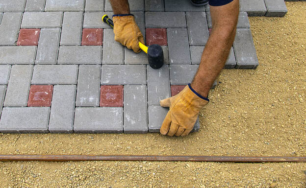 Professional bricklayers install new tiles for the patio on a foundation of lined sand in Norwalk, CT.